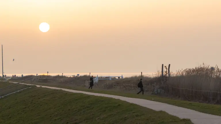 Sonnenaufgang mit Blick auf die Nordsee und den Deich mit Personen