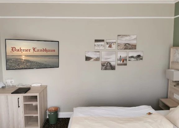 Blick in ein helles Hotelzimmer mit TV und Bilder im Hotel Duhner Landhaus